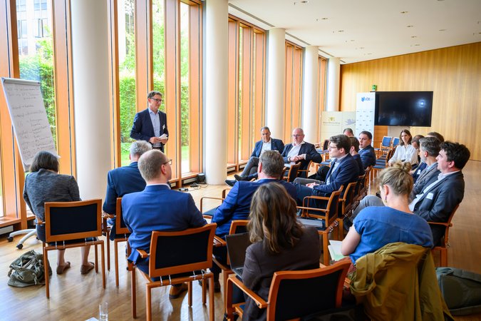 Öffnet eine Lightbox: Blick in einen Veranstaltungsraum, ein Mann hält eine Ansprache 