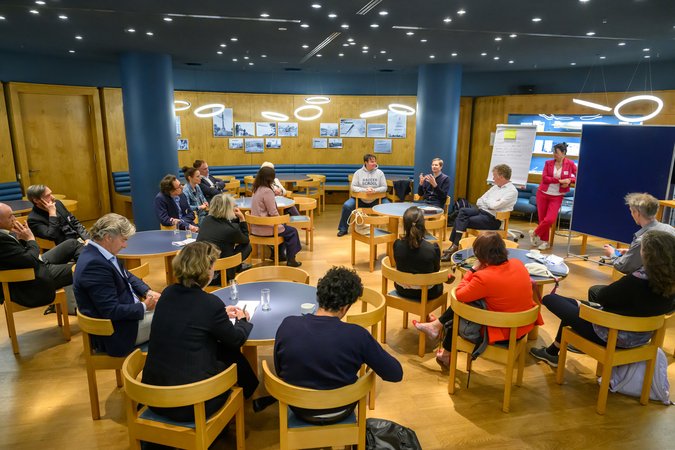 Öffnet eine Lightbox: Blick in einen Veranstaltungsraum, verschiedene Personen diskutieren 