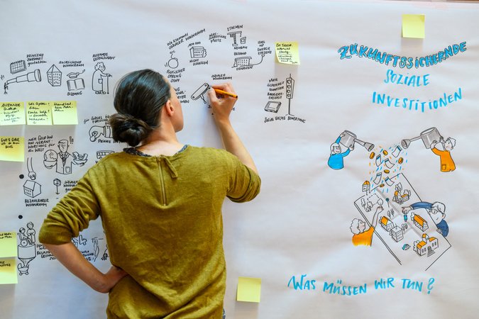 Öffnet eine Lightbox: Eine Frau schreibt etwas auf ein großes Papier 