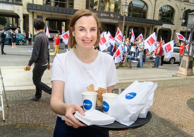Öffnet eine Lightbox: Anne Huning hält ein Tablett mit Speisen und Getränken Anne Huning